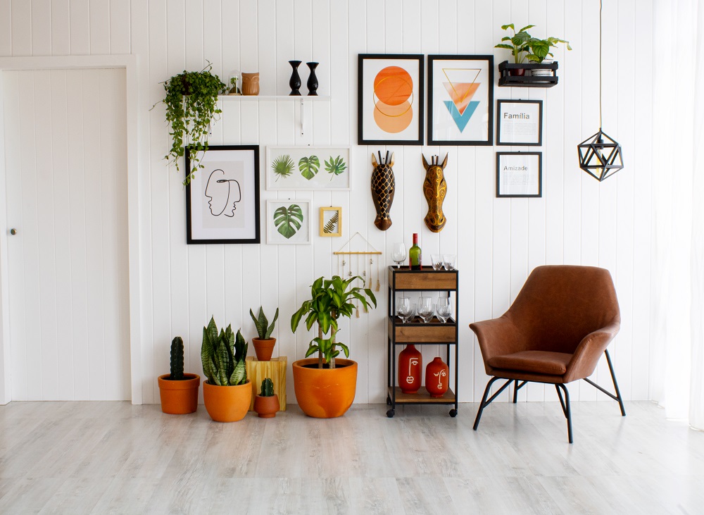 O ambiente possui uma parede cheia de quadros e elementos decorativos. No chão, há vasos de diferentes tamanhos, um carrinho bar e uma poltrona