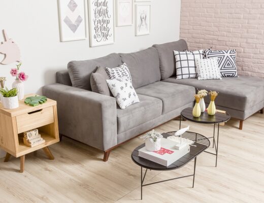 sala com sofá de canto cinza, mesa de centro, mesa lateral, almofadas, vasos e quadros decorativos