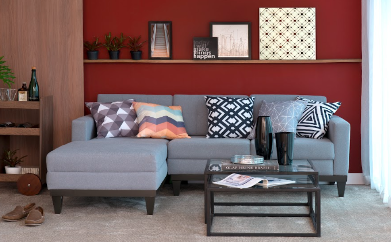 sofá para sala pequena com mesa de centro, carrinho-bar, prateleira com diversos itens decorativos e almofadas no sofá