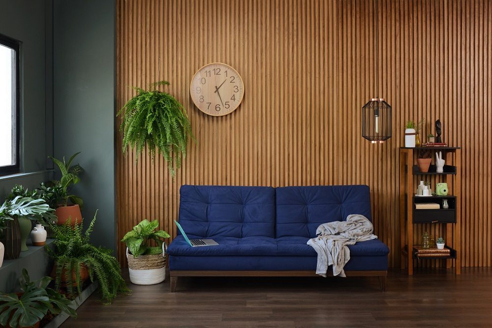 Sala de estar com um sofá azul no centro e parede lateral verde com diversas plantas