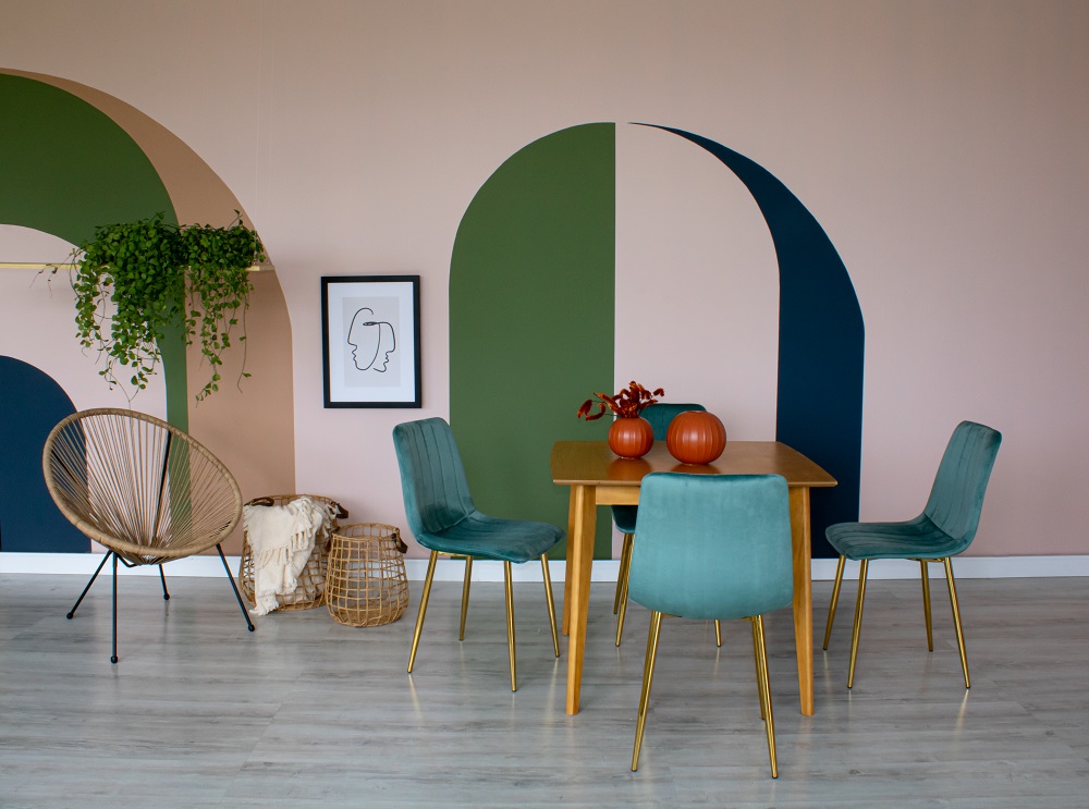 Sala de jantar com pintura orgânica ao fundo, cadeiras na cor verde e plantas