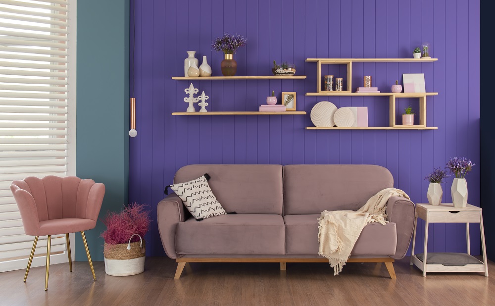 Sala de estar com cores da primavera como sofá e poltrona, rosas, parede roxa e móveis em tom de madeira clara