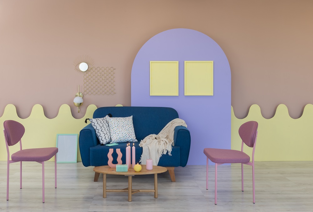 Sala de estar com diversas cores da primavera como o rosa e amarelo na parede, sofá azul, detalhes em roxo e almofadas claras.