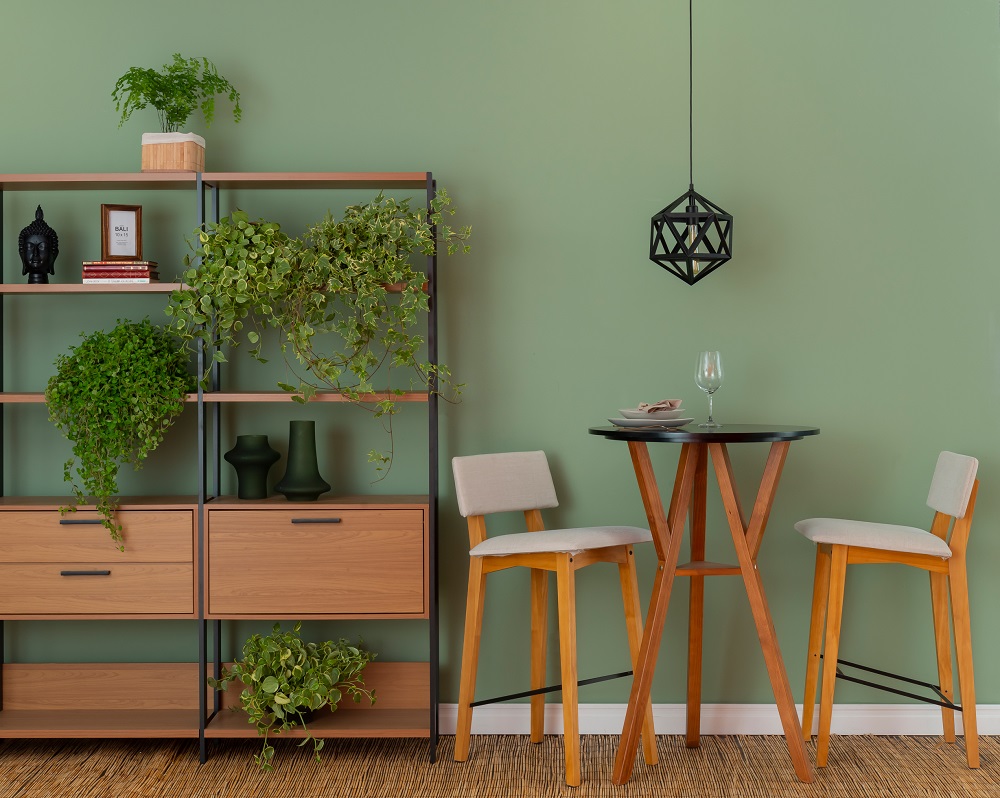 Sala de jantar com cores da primavera, sendo a parede ao fundo verde, os móveis em um tom de madeira médio e plantas espalhadas pela cena