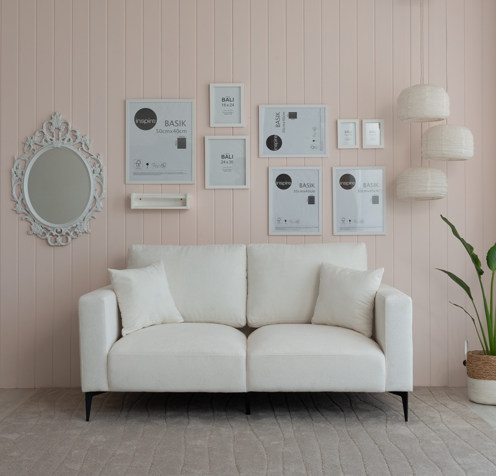 Sofá na Caixa Ubbe Lançamento Mobly. Na imagem, temos o sofá centralizado, ao fundo a parede rosa e quadros brancos pendurado. No lado direto, há um vaso de planta e pendentes de luz.