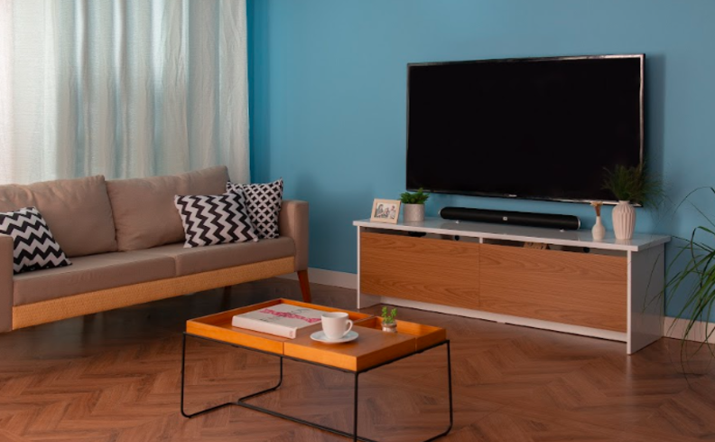 sala de estar com rack de madeira, sofá, mesa de centro, almofadas e itens de decoração