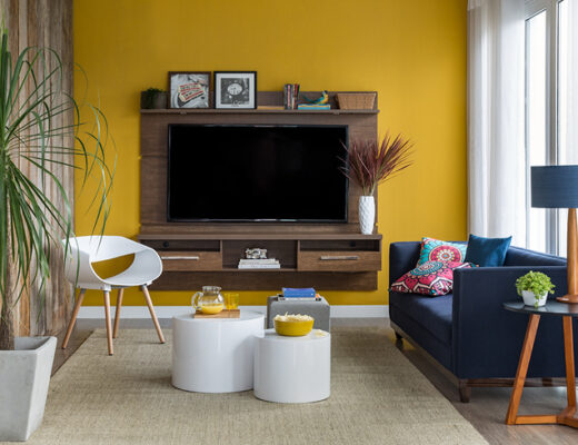rack e painel para sala na cor marrom, com TV, sofá, puffes, poltrona e diversos itens decorativos