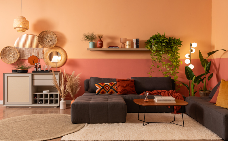 decoração para sala de estar pequena com sofá em L, mesa de centro, prateleiras e diversos itens decorativos como plantas, livros e quadros