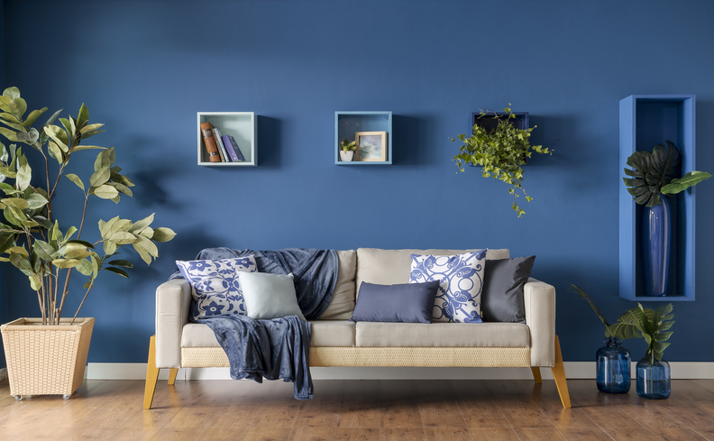 sofá para sala pequena em um ambiente com parede azul, nichos, sofá fixo cinza e diversas almofadas e mantas