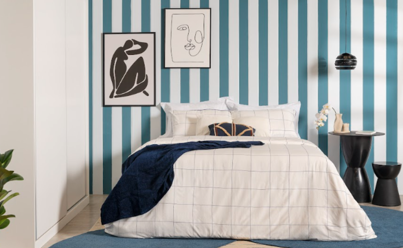cores para quarto azul e branco com parede pintada, além de roupa de cama branca e preta, quadros decorativos e luminária