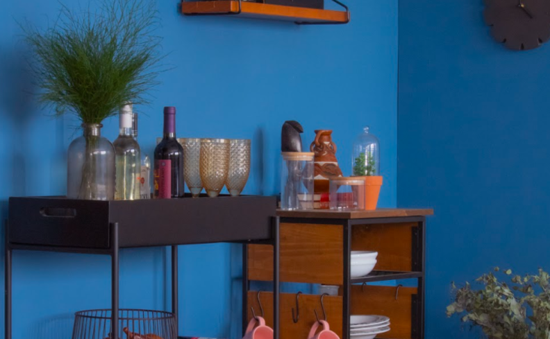 parede de sala de estar pintada em tons de azul escuro com um carrinho bar preto com bebidas e um em madeira.