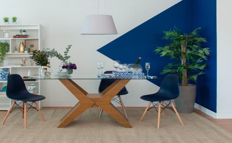 tons de azul escuro com branco em uma sala de jantar com cadeiras, mesa e estante, além de um vaso com plantas e lustre.