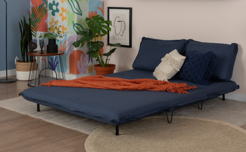 sofá cama retrátil azul aberto em uma sala de estar com almofadas e manta