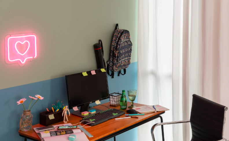 cortina para home office de tecido claro, além de escrivaninha, itens de escritório, cadeira e itens decorativos.