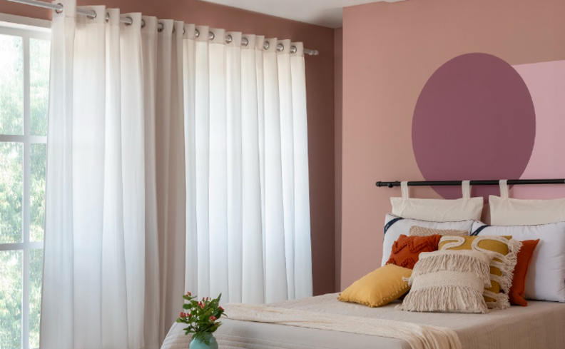 cortina para usar no quarto em um modelo de tecido em tom claro, além de cama posta com edredom, almofadas e travesseiros.