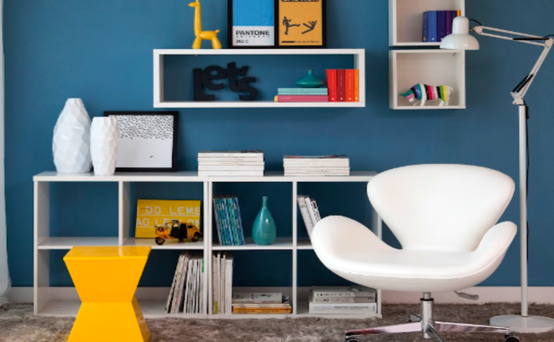 poltrona de leitura em um ambiente com estante na horizontal, luminária de chão, banco, nichos e diversos itens de decoração.