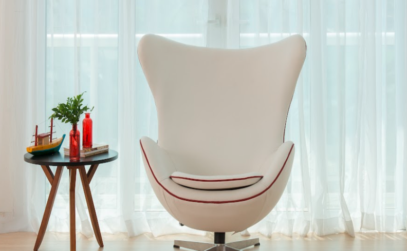 poltrona orgânica branca na sala de estar, além de mesa de apoio e itens decorativos como vela e vaso com plantas.