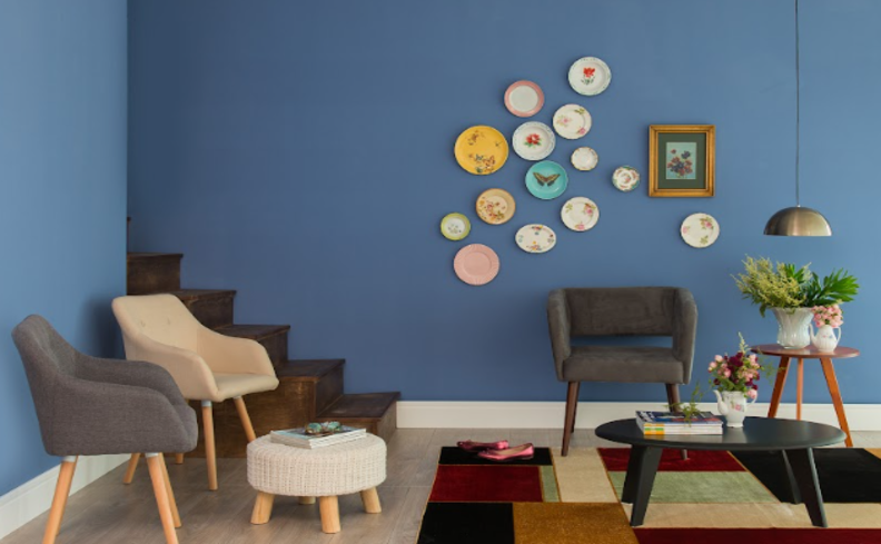 ambiente com duas poltronas decorativas, puffe, mesa de centro, tapete e diversos quadros na parede.