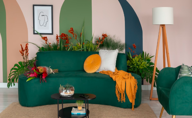 sofá orgânico na sala de estar, com almofadas e manta, além de mesa de centro, luminária de chão e diversas plantas decorativas.