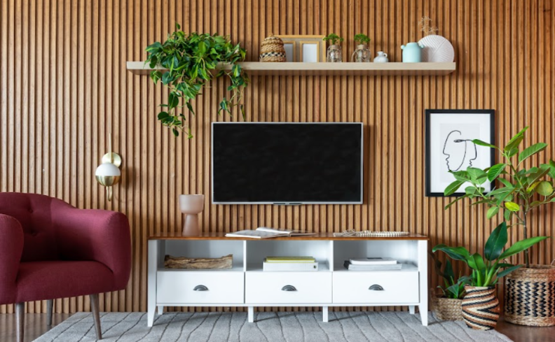 decoração de sala com plantas naturais, além de rack de madeira, painel ripado, poltrona e outros itens decorativos.
