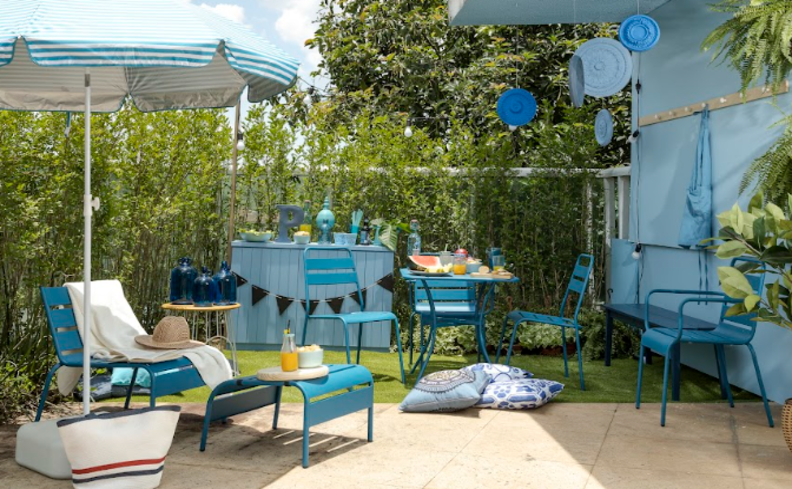 tons de azul na decoração aesthetic da varanda com mesas, cadeiras, bancos e almofadas, além de outros itens decorativos.