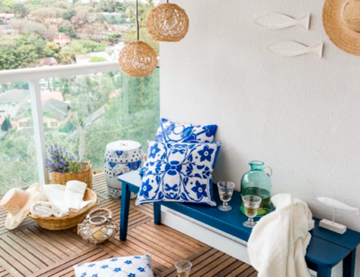 móveis para área externa de apartamento com banco, almofadas em tons de azul, manta para sofá, lustres pendentes e outros itens decorativos.