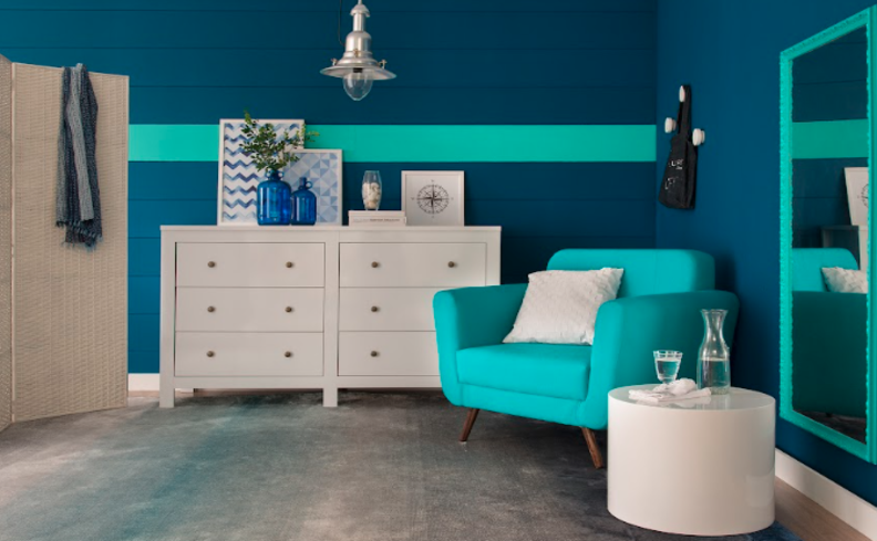 duas cômodas para sala brancas, além de poltrona azul, mesa de apoio branca e itens decorativos como vasos, quadros e livros.