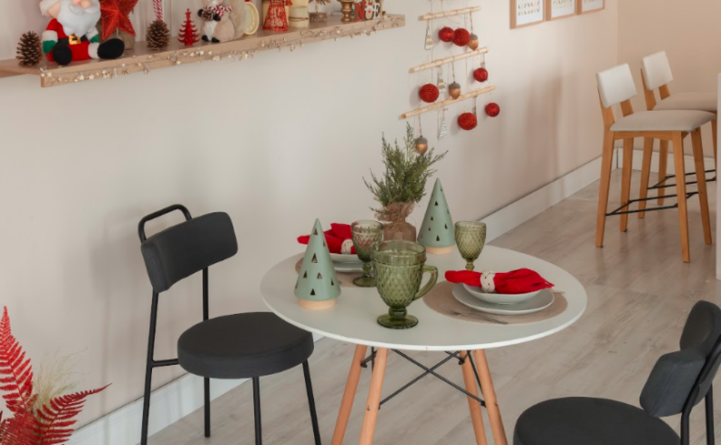 mesa posta de natal simples com mesa branca resonda, duas cadeiras pretas, taças verdes, pratos e guardanapo de tecido vermelho.