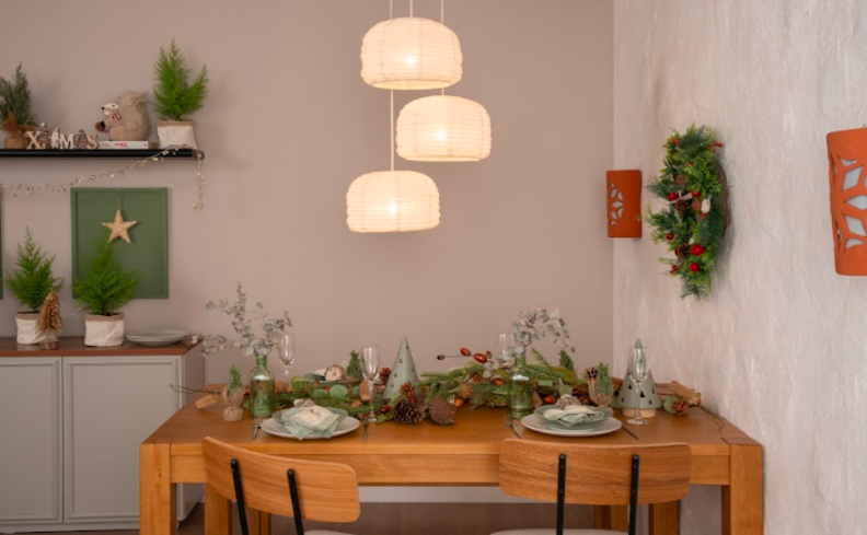 mesa posta de natal com mesa retangular de madeira, cadeiras, lustre, pratos brancos, taças, talheres e diversos itens decorativos.