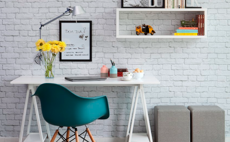 cantinho de estudo no quarto com escrivaninha branca, cadeira de escritório azul, estantes brancas e dois puffes cinzas.