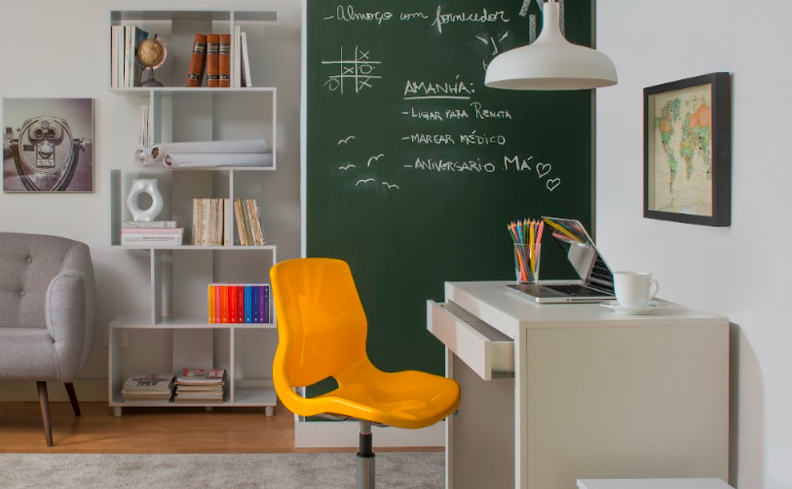 cantinho de estudo simples em casa com escrivaninha, cadeira de escritório, prateleira e uma parede lousa.