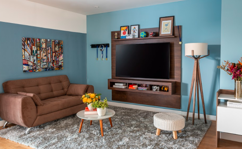 cor de parede de sala moderna com tons de azul e móveis em tons de marrom, além de itens decorativos em cores neutras para criar equilíbrio na composição.