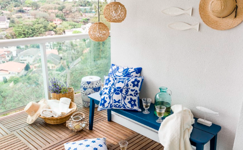 cores de tinta para varanda, com parede branca, banco com azul e branco, além de diversas almofadas, mantas, lustres pendentes e outros itens de decoração.