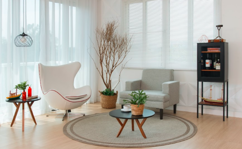 cores neutras para a decoração da casa, em um ambiente com duas poltronas, tapete, estante, mesa de apoio e diversos itens decorativos.