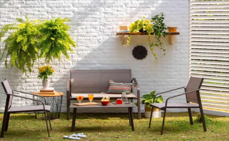 decoração em varanda com sofá, poltronas, mesa de apoio e estante. Além de diversas plantas e adornos decorativos.