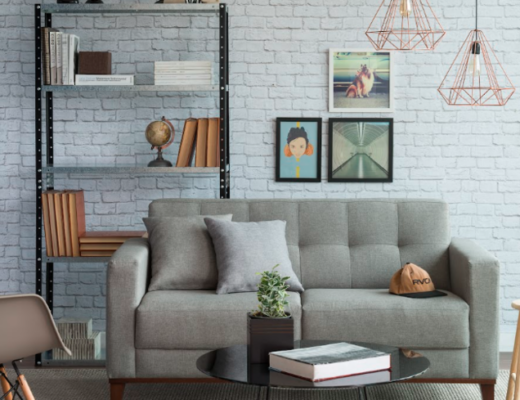 sala de estar no estilo industrial com sofá cinza, estante de metal preto, lustres pendentes, quadros e parede de tijolinhos.