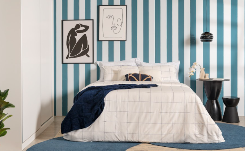 quarto de casal decorado com tons de azul e branco, além de quadros decorativos, mesa de cabeceira e adornos.