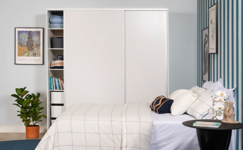 dicas para deixar o quarto organizado, com cama posta, guarda-roupa arrumado por cores, além de itens decorativos como planta, quadros e mesa lateral.