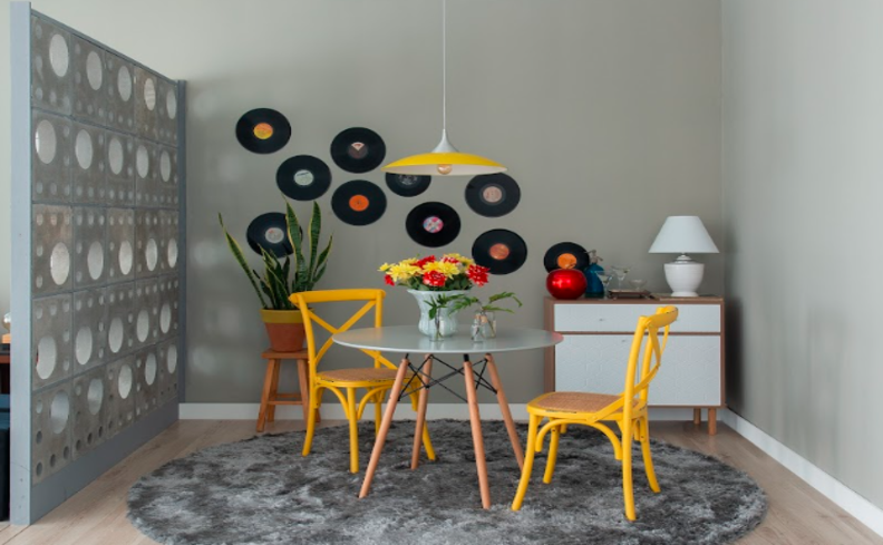 tapete para sala de jantar com mesa redonda, cadeiras amarelas, mesa de apoio e discos de vinil pendurados na parede.