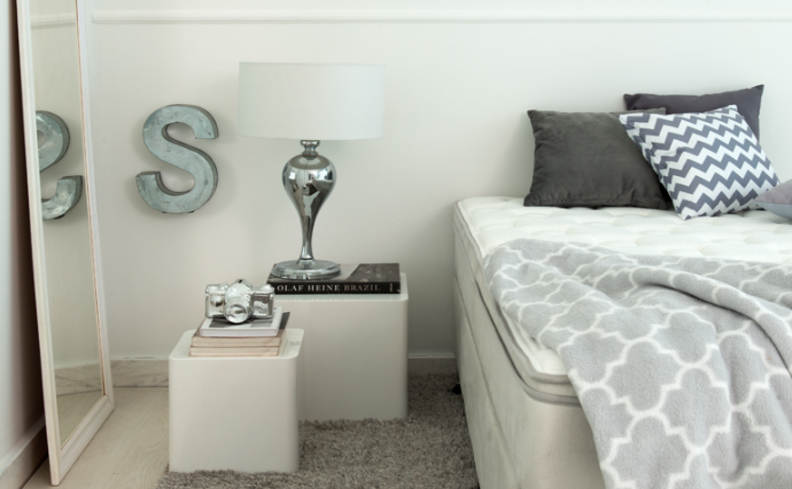 dicas para saber como escolher luminária para quarto com uma decoração moderna e simples em tons de branco, cinza e preto. Com cama, mesa de cabeceira, luminária de mesa e adornos decorativos.