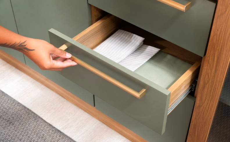 cozinha modulada pequena com diversas gavetas para atender as necessidades do dia a dia. Gaveta aberta na cor verde e madeira claro.