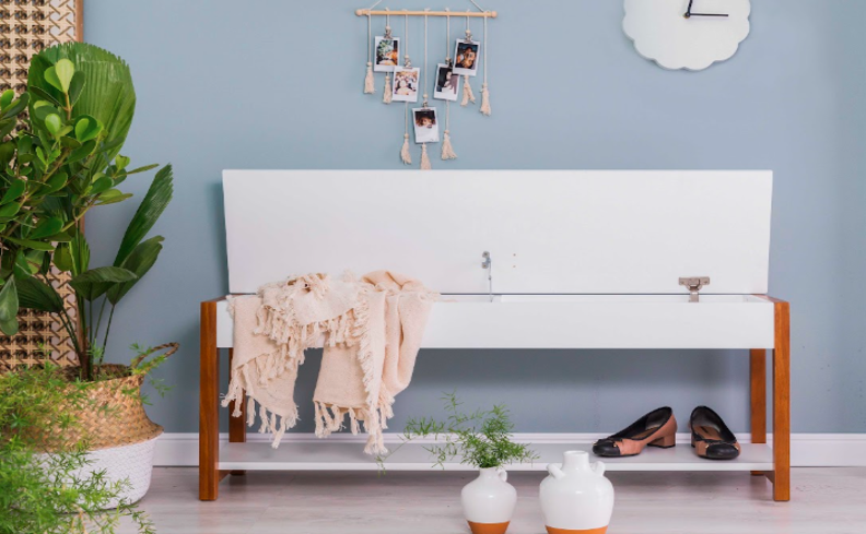 mini sapateira para hall de entrada em um modelo com tampa de abre para cima, na cor branca, vasos com plantas e itens decorativos nas paredes.