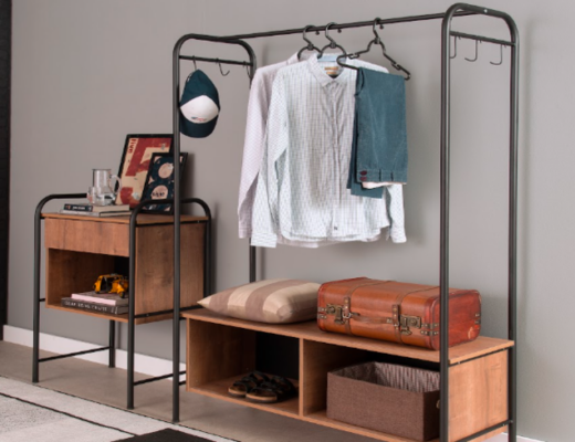 arara de roupas para quarto com modelo em aço preto, além de mesa de cabeceira e diversas peças de roupas penduradas nesse móvel para facilitar a rotina.