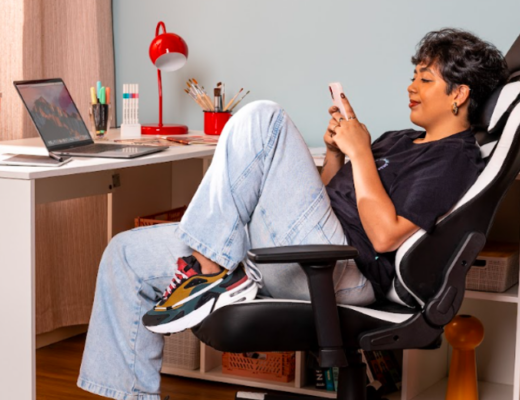 mulher sentada em uma cadeira gamer em um home office mexendo no celular procurando boas ofertas para aproveitar o mês do consumidor.