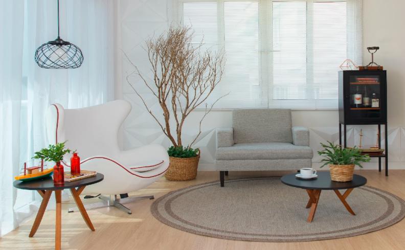 salas decoradas pequenas e modernas com poltrona branca e uma cinza, tapete redondo, estante pequena, vaso com plantas e uma paleta de cores neutras para compor a decoração.