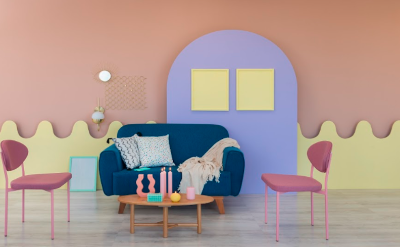 apartamento decorado na sala de estar com parede rosa e azul, poltronas, sofá azul, mesa de centro e diversas almofadas decorativas.