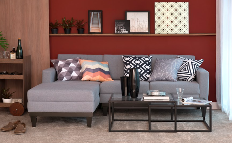 decorar apartamento alugado com sala de estar com sofá cinza, parede em um tom de vinho, prateleira com diversos quadros encostados na parede, mesa de centro e um carrinho bar ao lado do sofá.