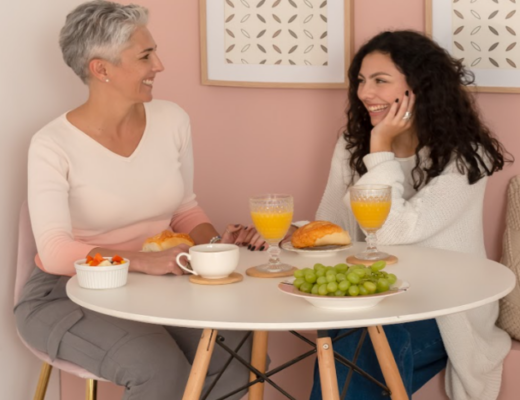 mesa posta dia das mães com mãe e filha sentadas ao redor de uma mesa redonda tomando um café da manhã especial para comemorar essa data.