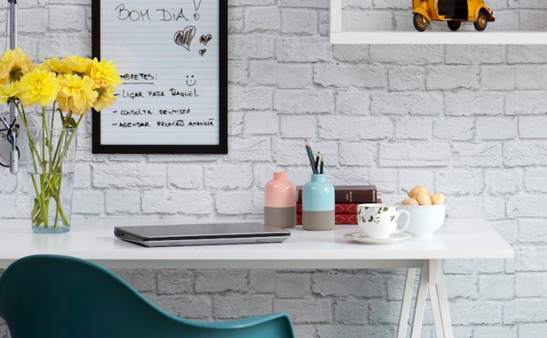 mesa de altura regulável branca, com cadeira de escritório verde e itens de decoração como vaso e quadro para complementar o home office.