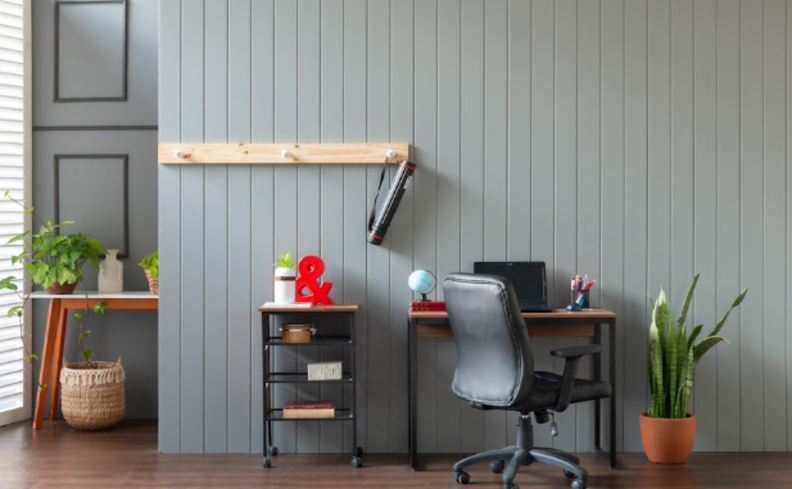 mesa ergonômica ajustável no home office com cadeira de escritório, estante, vasos com flores e um carrinho auxiliar.